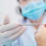 Close-up image of dentis using small mirror and carver when examining teeth of male patient.