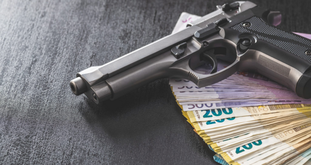 Hand gun and euro banknotes on black table.